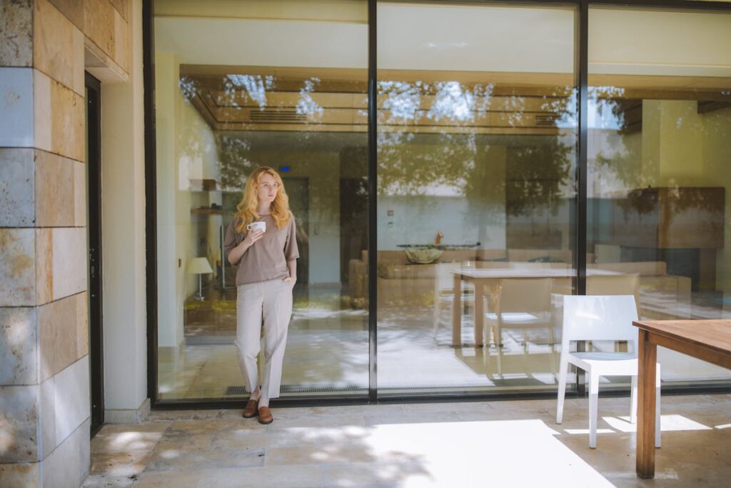 A person standing by a window, sipping tea and looking outside mindfully.

